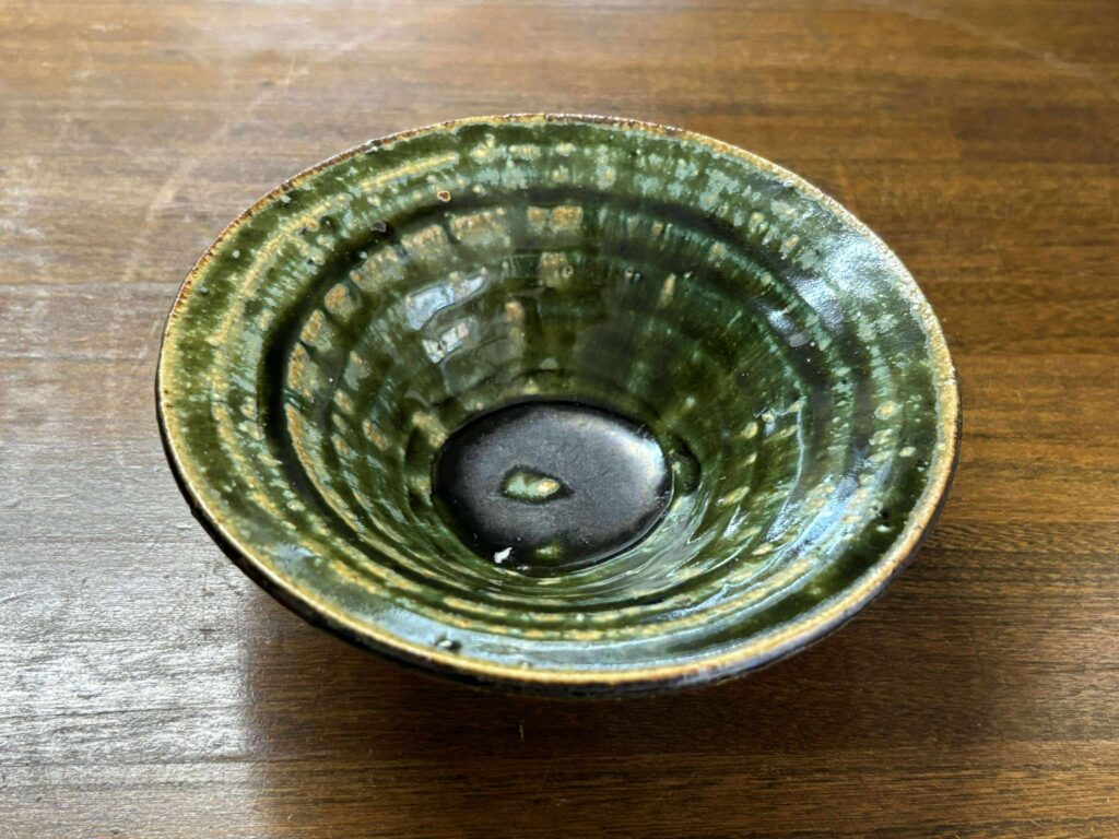 深い緑釉の陶器の小鉢が写っています。内側には轆轤(ろくろ)の跡が美しく残っており、自然な揺らぎや釉薬の濃淡が味わい深い一品です。和風の趣があり、手仕事の温もりが感じられる器です。